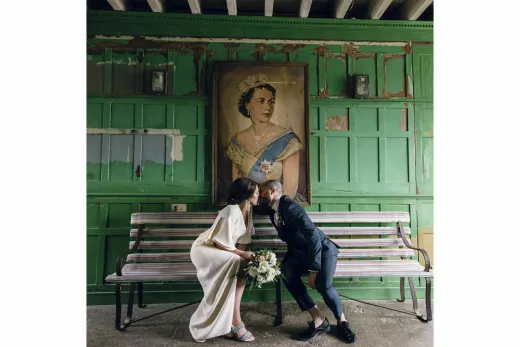 A bride and groom kissing on a bench in front of a painting.
