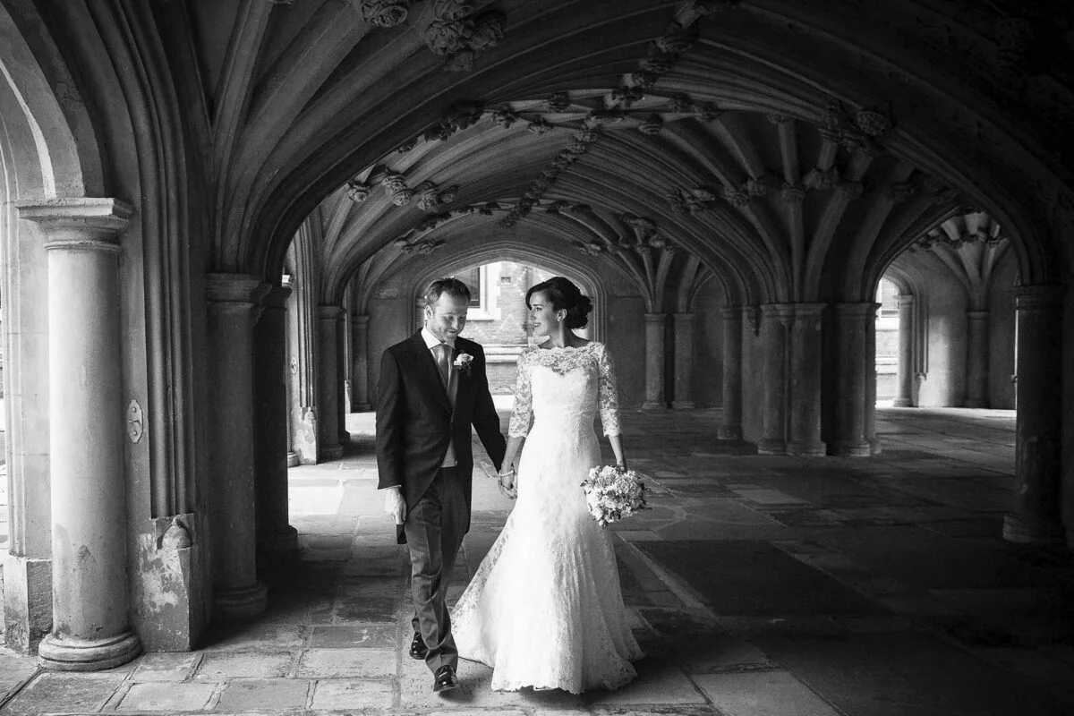 A bride and groom standing under arches in a black and white photo.