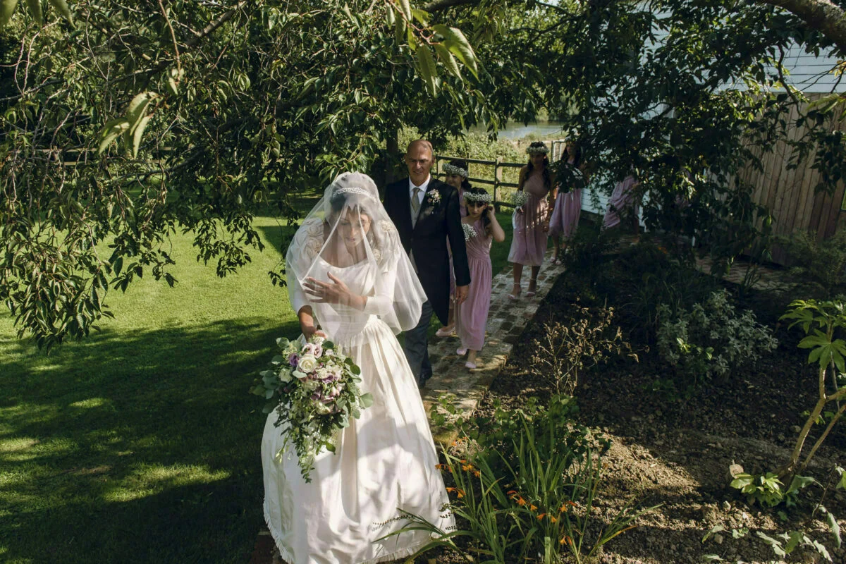 A bride and her bridesmaids walk through a garden.