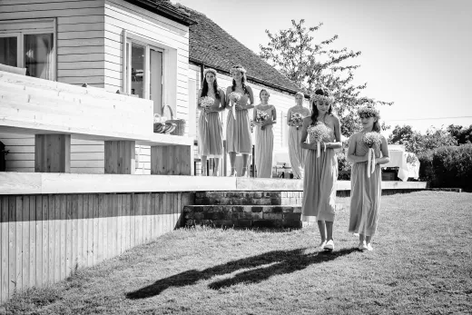 Black and white photo of bridesmaids walking in front of a house.