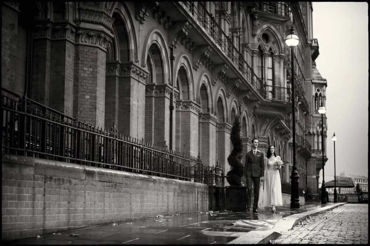 A bride and groom standing on a wet street.