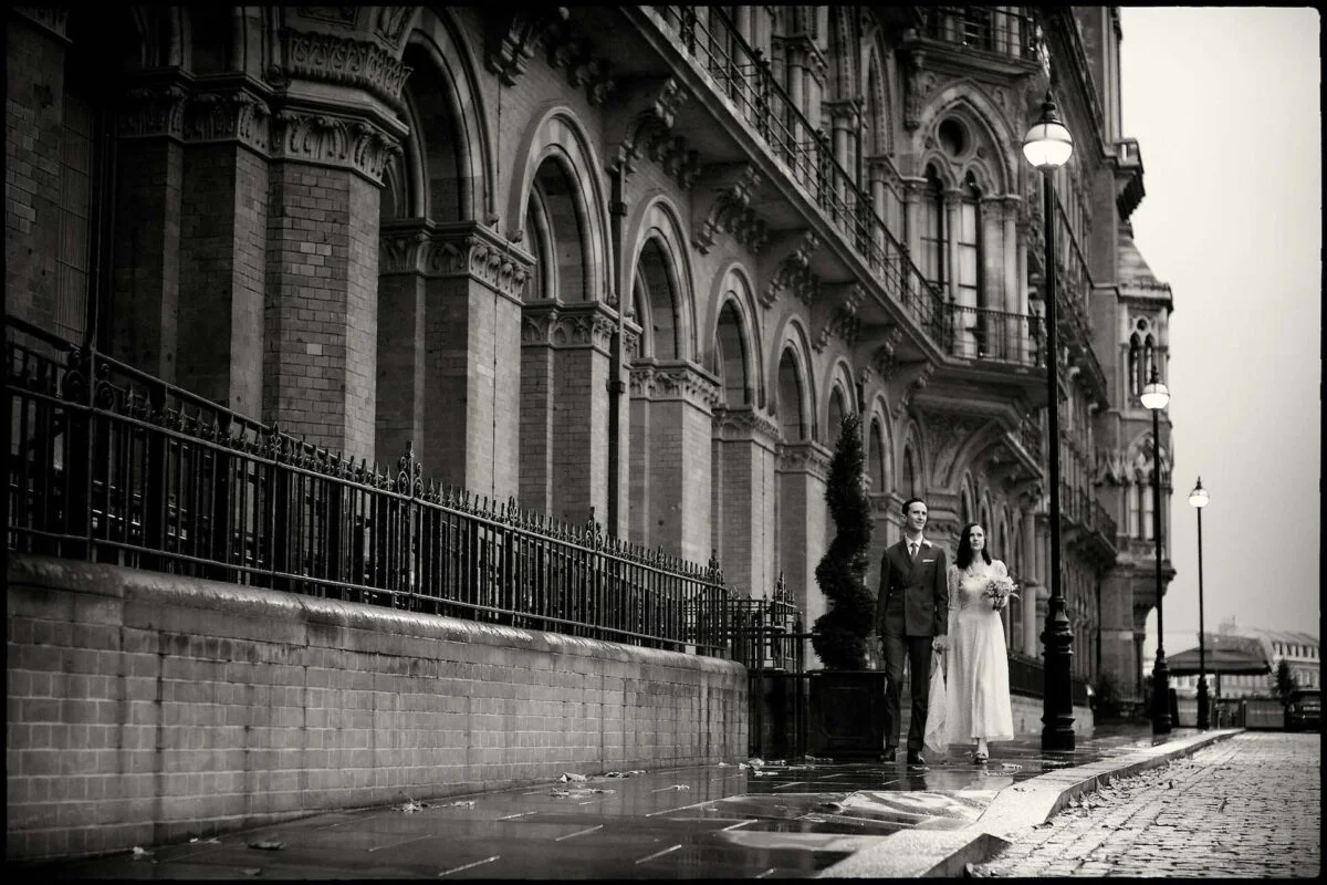 A bride and groom standing on a wet street.