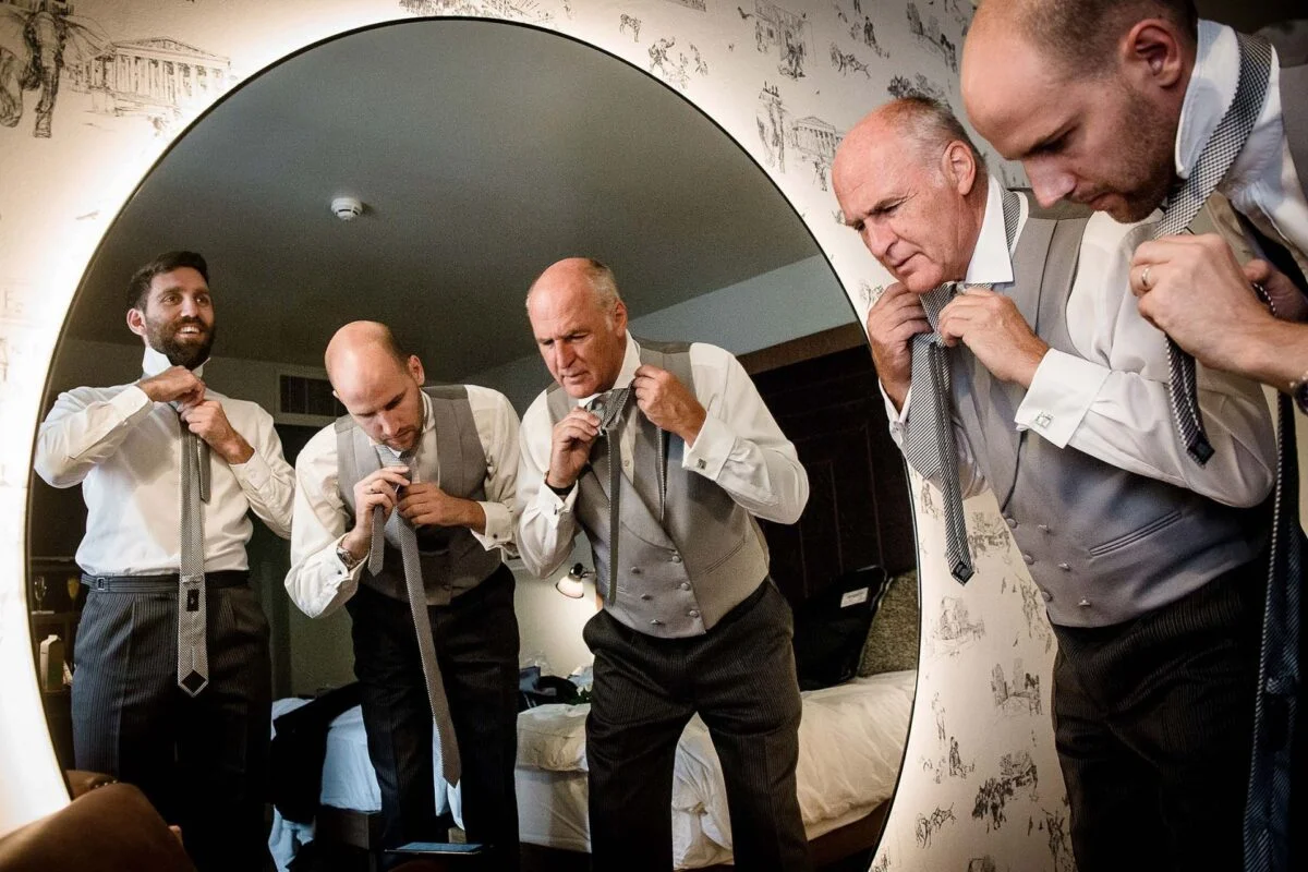 A group of men are adjusting their ties in front of a mirror.