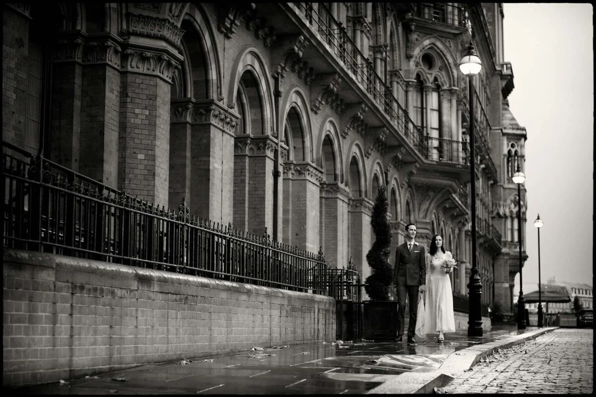A bride and groom standing on a wet street.