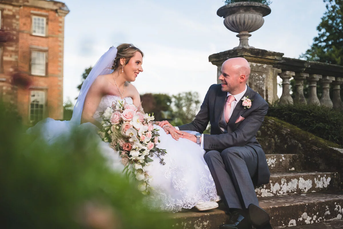 A bride and groom sitting on steps in front of a mansion.