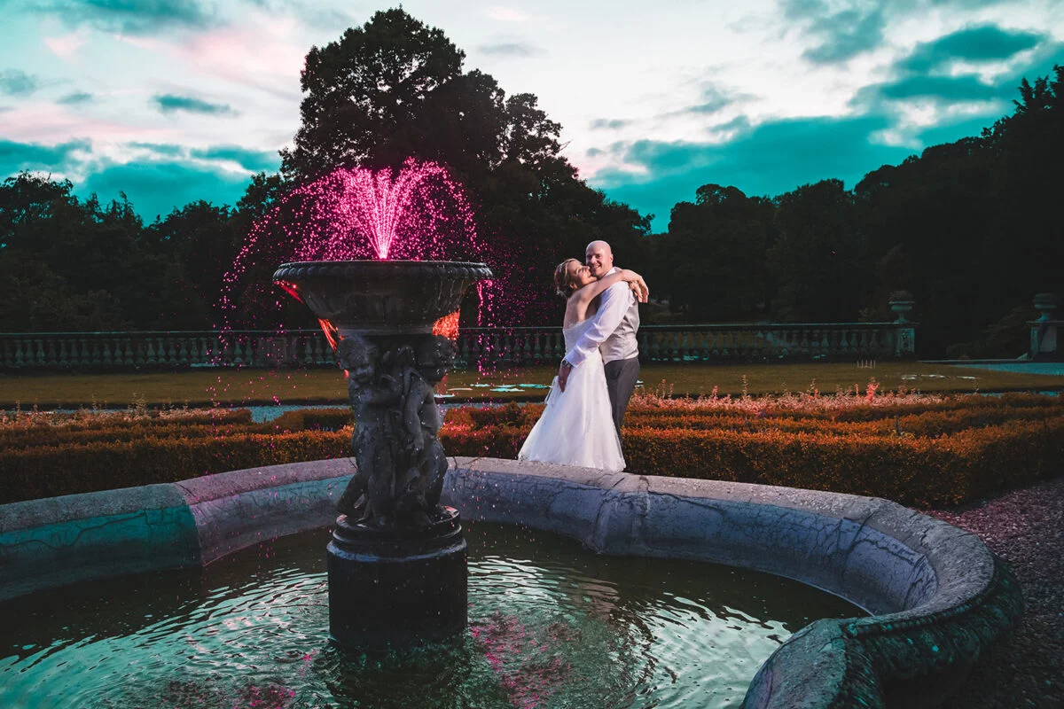 A bride and groom posing in front of a fountain.