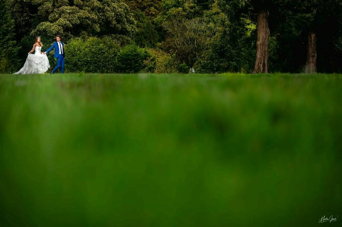 A bride and groom walking in a grassy field.