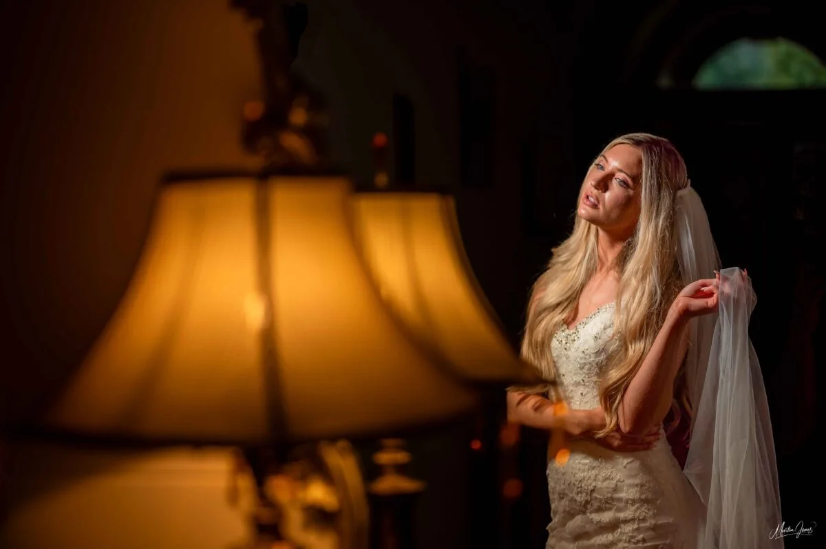 A bride posing in front of a lamp in a dark room.