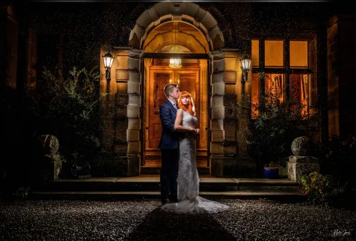A bride and groom standing in front of a mansion at night.