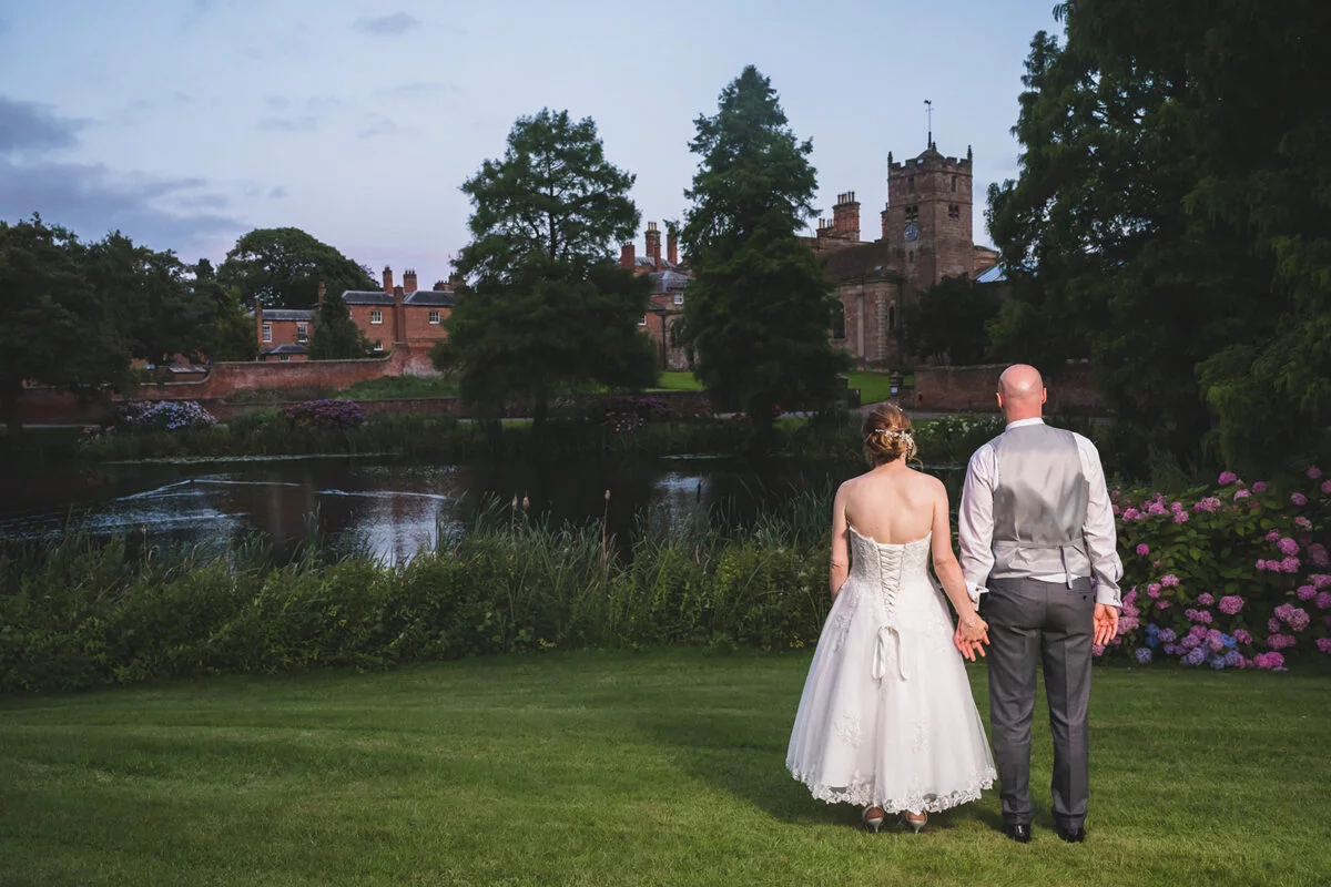 A bride and groom standing in front of a castle at dusk.