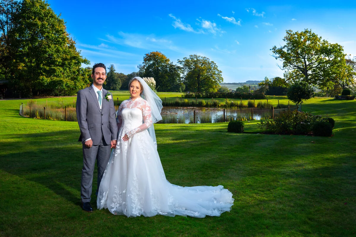 A bride and groom posing in front of a pond.