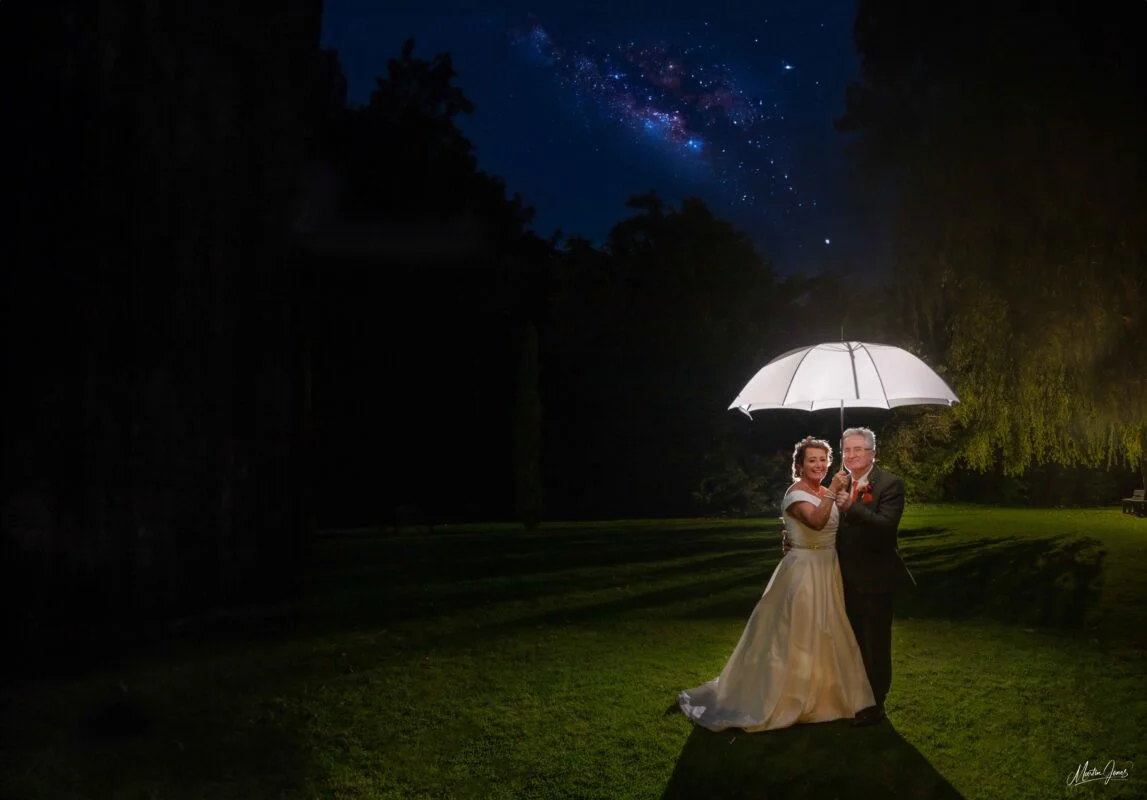 A bride and groom standing under an umbrella.