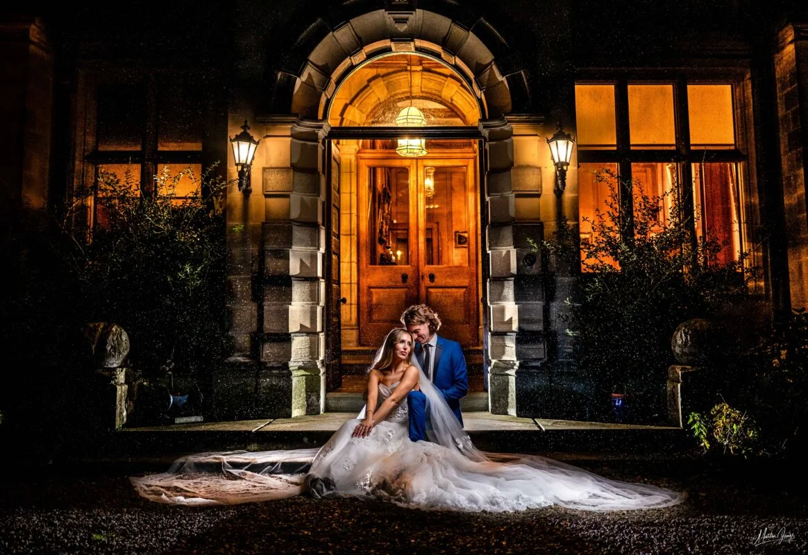 A bride and groom sitting on the steps of a mansion at night.