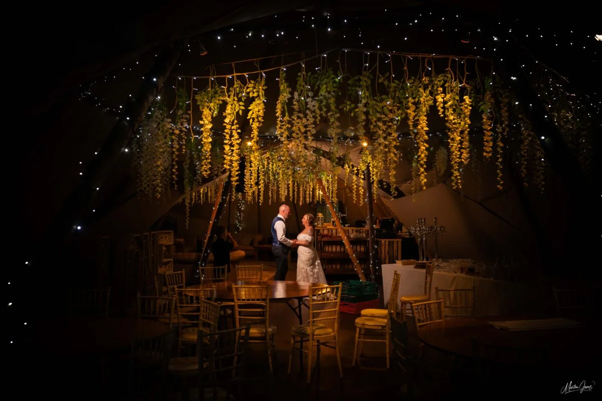 A bride and groom standing under a tent with flowers hanging from the ceiling.