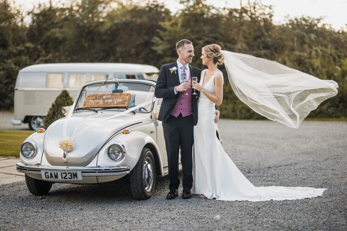 A bride and groom standing next to a volkswagen beetle.