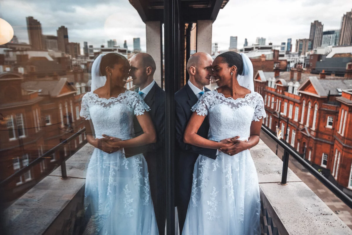 A bride and groom standing in front of a window in london.