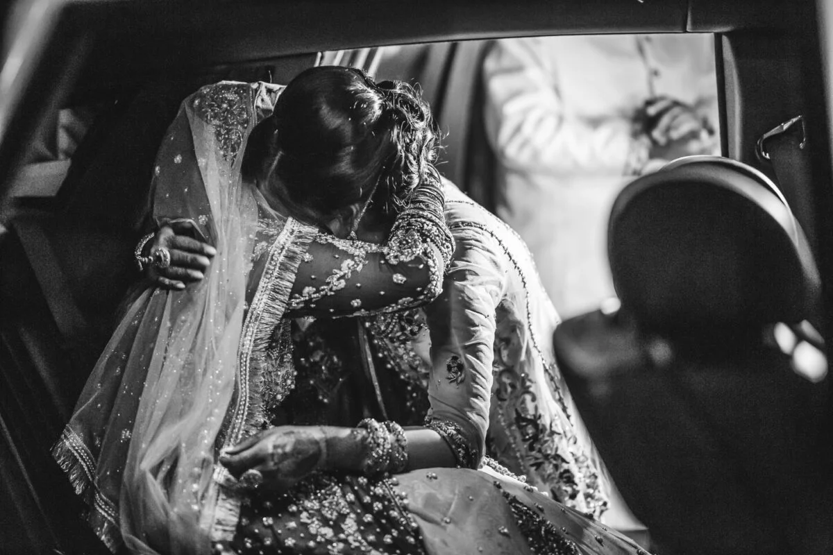A bride is hugging her bridesmaid in the back seat of a car.
