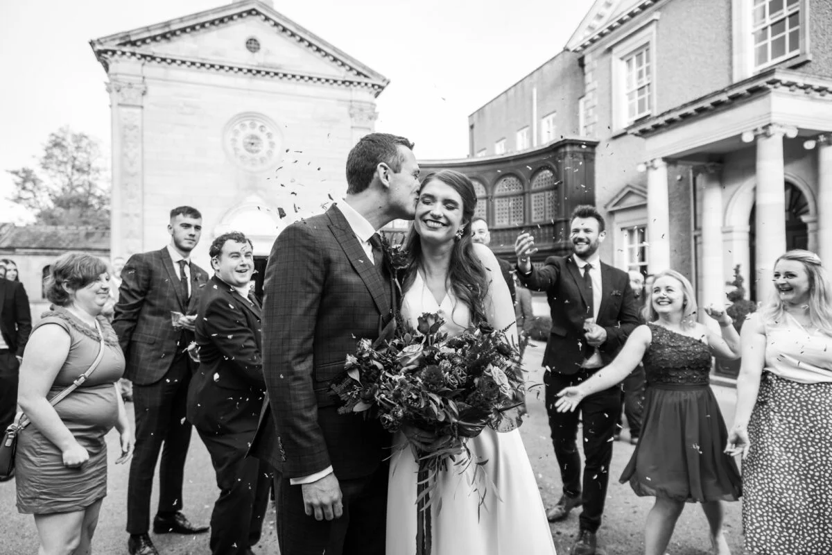 A black and white photo of a bride and groom with confetti thrown at them.