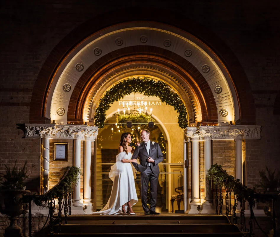 A bride and groom standing in front of an archway at night.