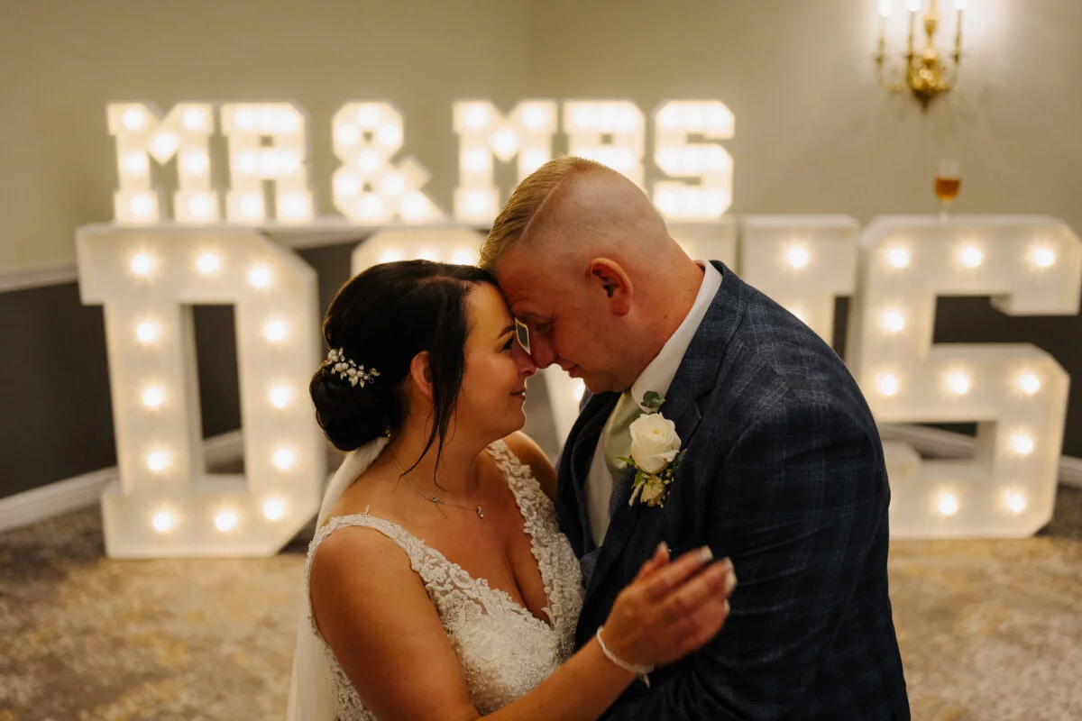 A bride and groom embracing in front of a mr and mrs sign.