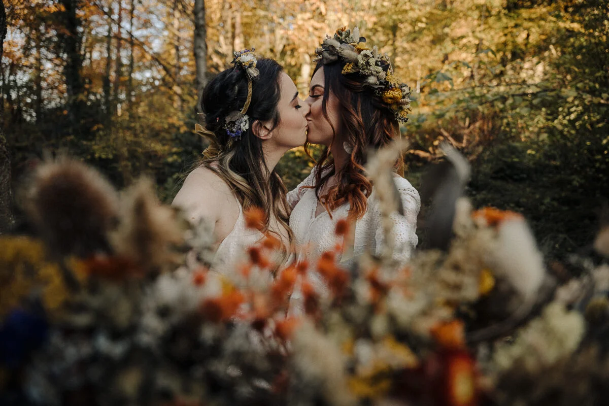 Two brides kissing in the woods.