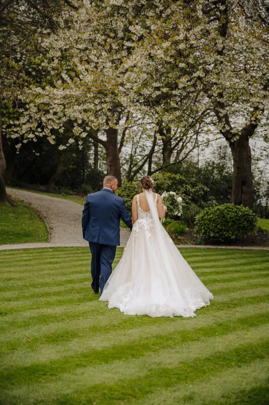 A bride and groom walking through a flowering garden.