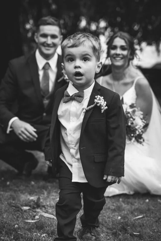 A black and white photo of a little boy walking with his bride and groom.