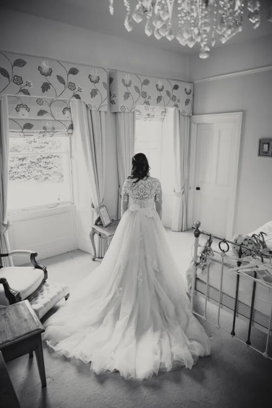 A bride looking at her wedding dress in a bedroom.