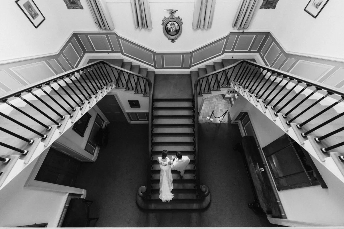 A black and white photo of a bride standing on a staircase.