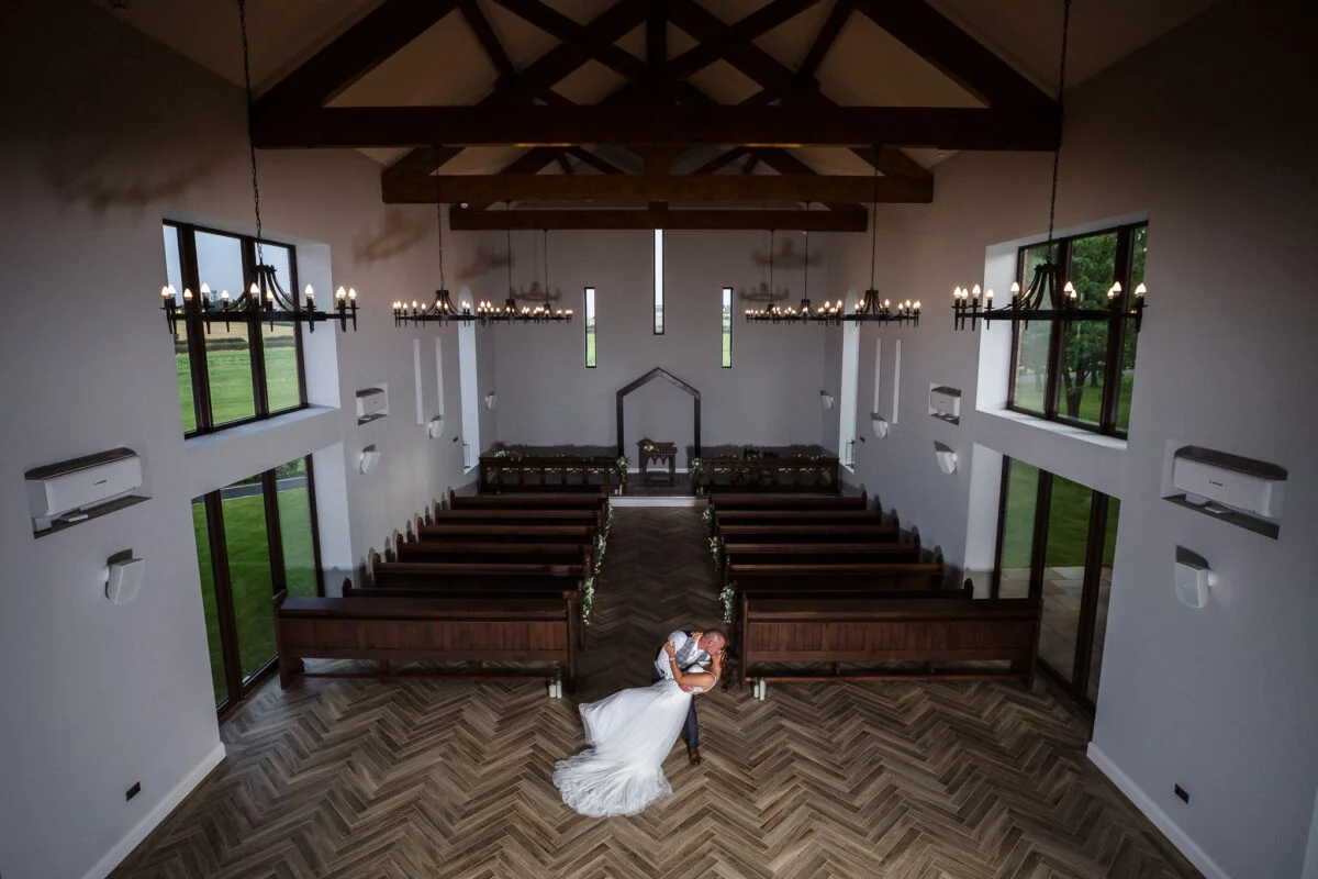 A bride and groom standing in a church with wooden pews.