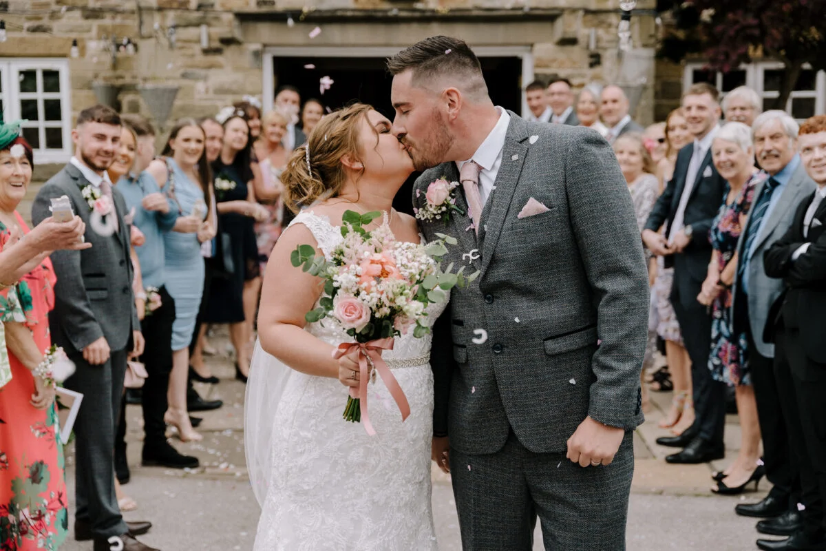 A bride and groom kissing in front of confetti.