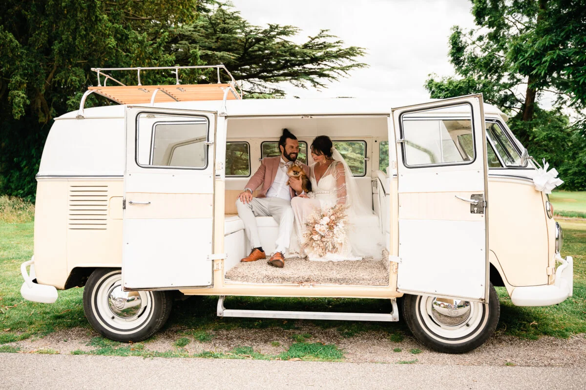 A bride and groom sit in the back of a vw camper van.