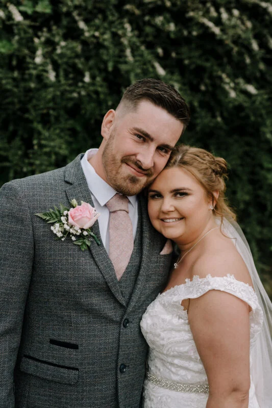 A bride and groom posing for a photo in front of bushes.