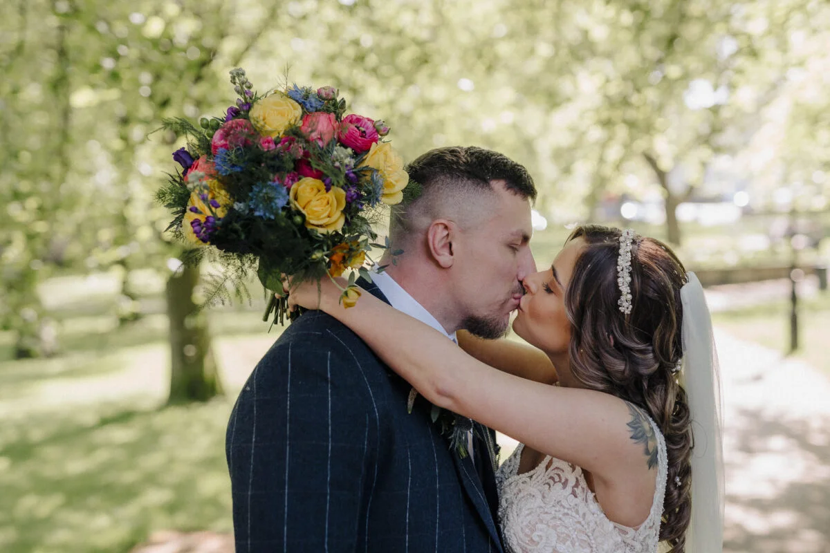A bride and groom kissing under a tree in a park.
