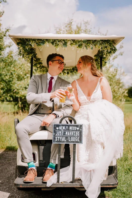 A bride and groom sitting in a golf cart.