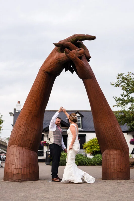 A bride and groom standing in front of a large wooden sculpture.