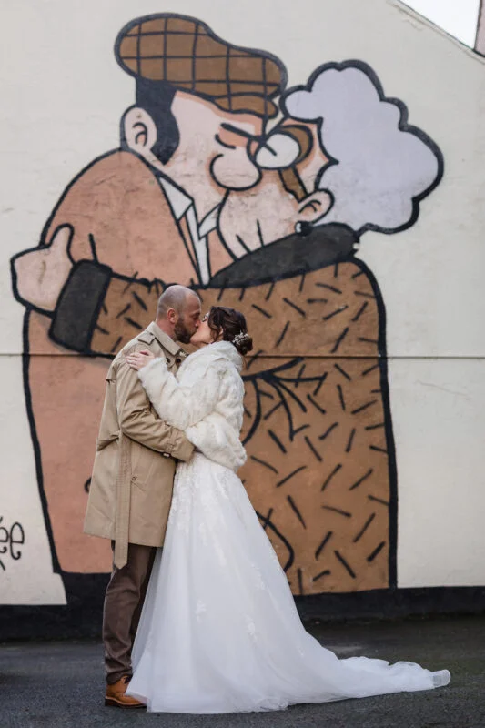 A bride and groom kiss in front of a mural.