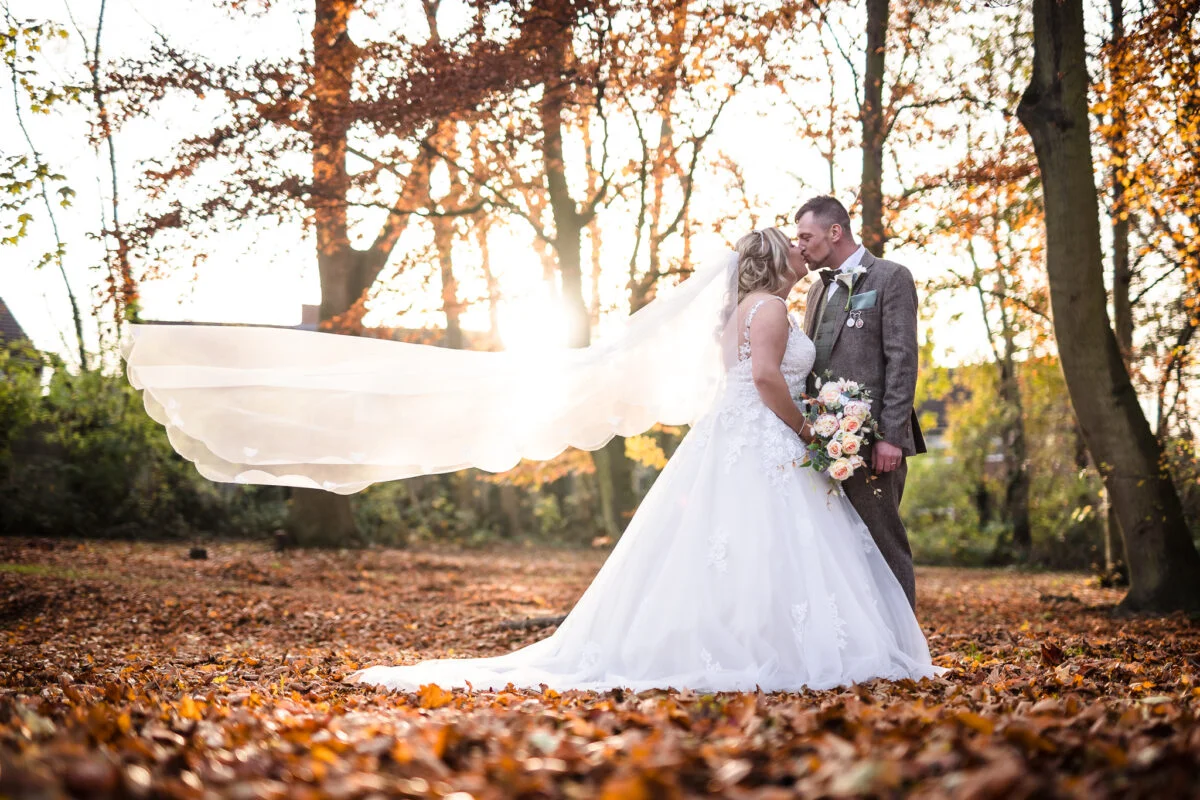 A bride and groom kissing in the autumn leaves.