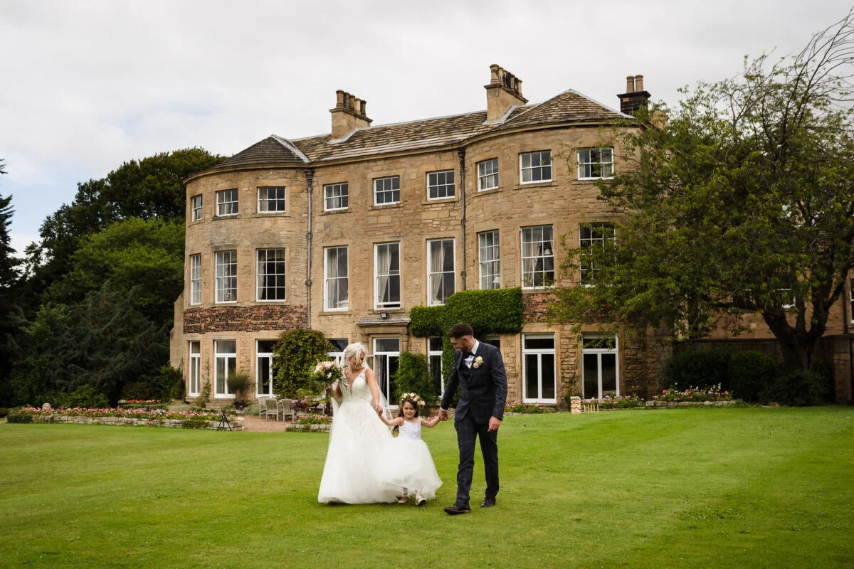 A bride and groom walking in front of a large mansion.