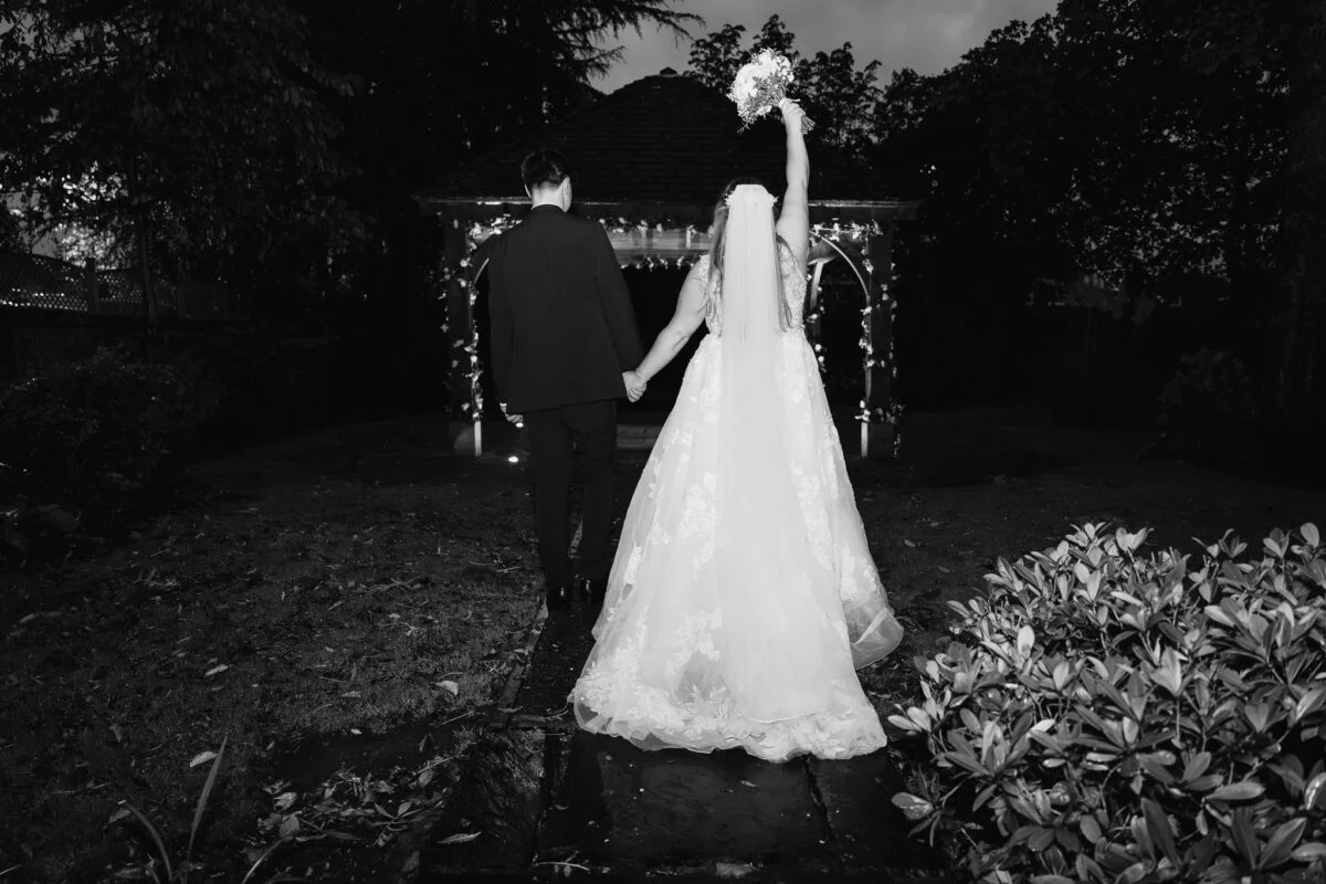 A bride and groom walking through a gazebo at night.