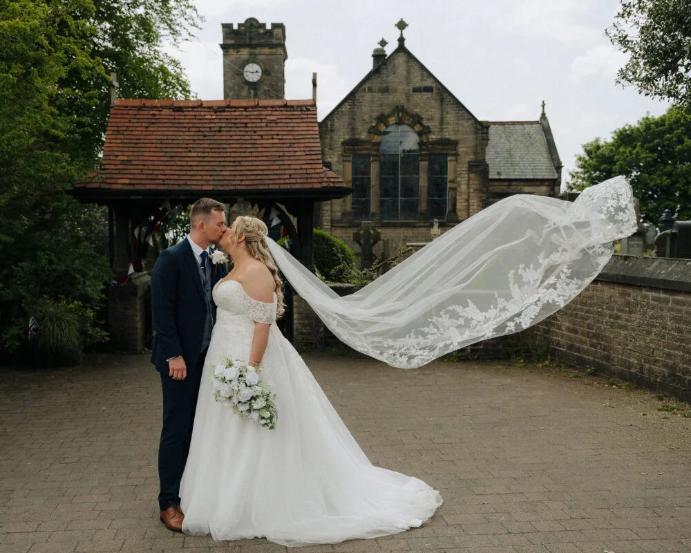 A bride and groom kissing in front of a church.