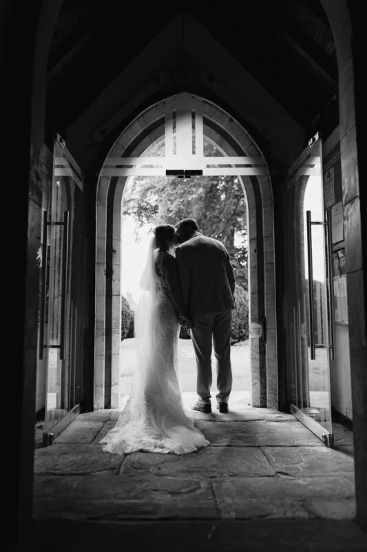 A bride and groom standing in the doorway of a church.