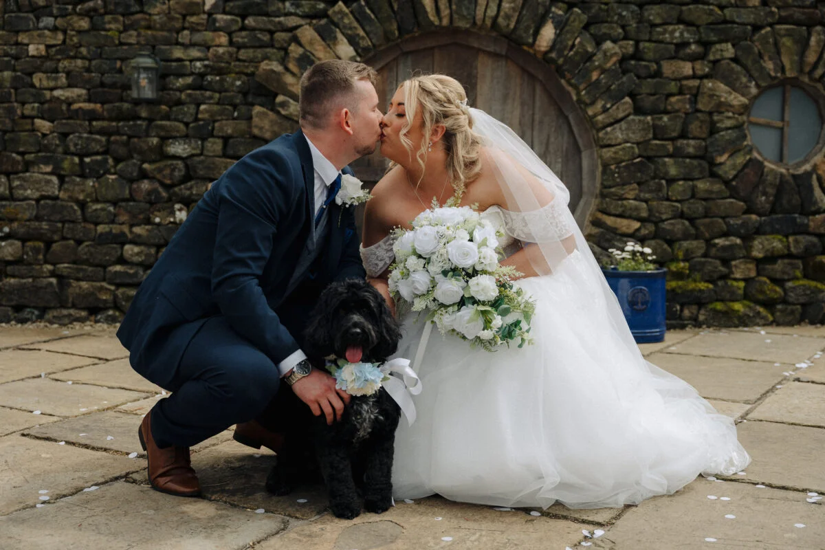 A bride and groom kissing in front of a stone wall.