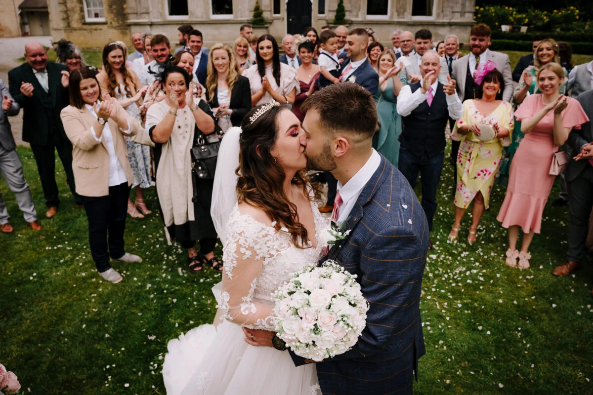 A bride and groom kissing in front of a crowd of people.