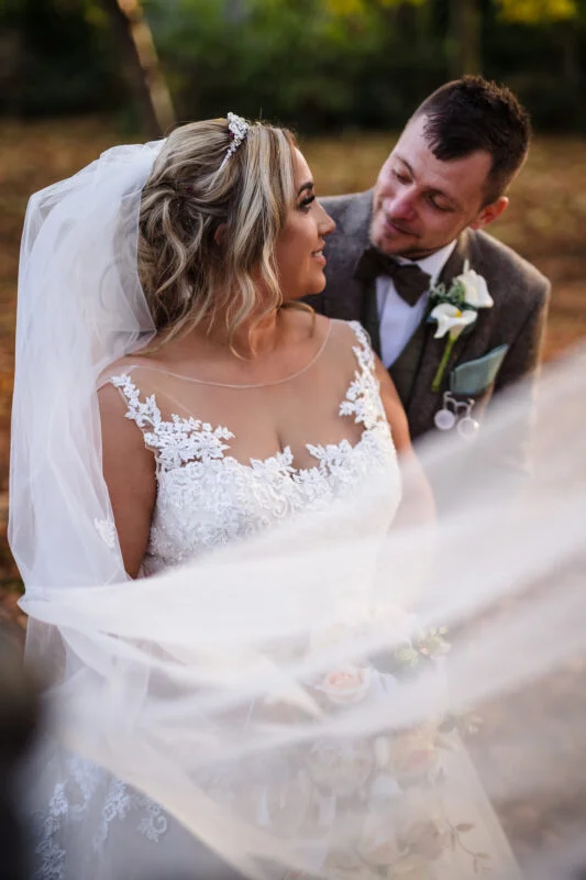 A bride and groom kissing under a veil in the woods.