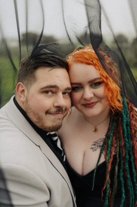 A man and woman posing for a photo under a veil.