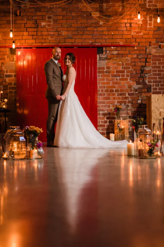 A bride and groom standing in front of a red brick wall.