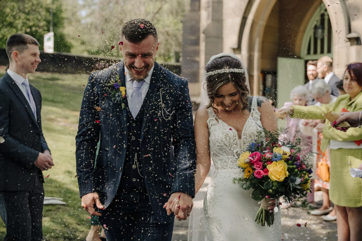 A bride and groom walk out of a church with confetti thrown at them.