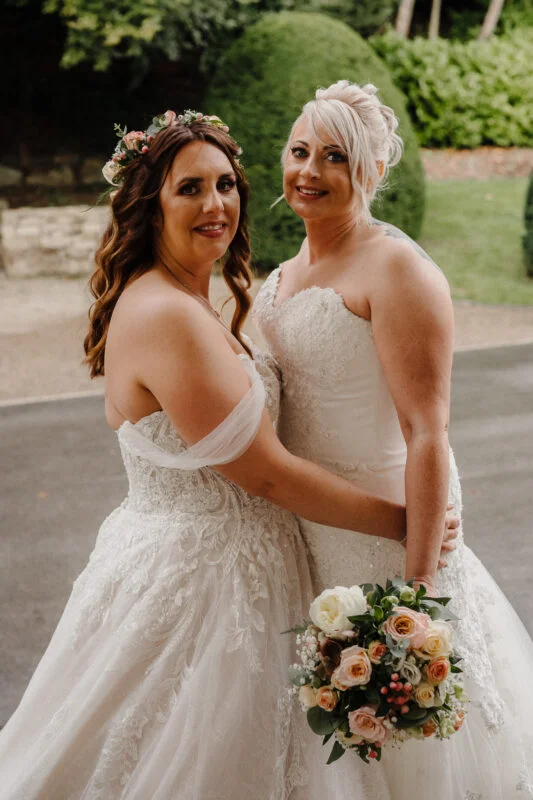 Two brides posing for a photo in their wedding dresses.