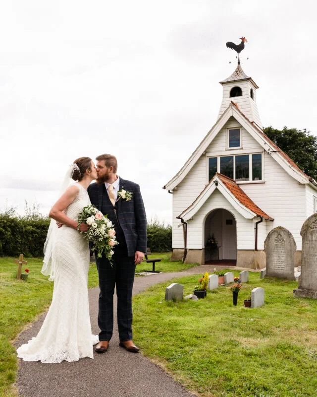 A bride and groom kiss in front of a small church.
